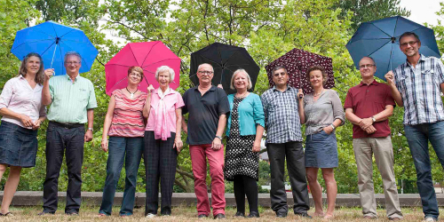Mitglieder des Vereins stehen nebeneinander mit Regenschirmen