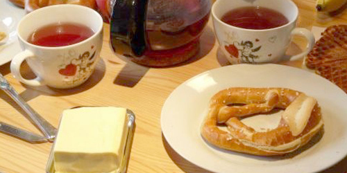 gedeckter Frühstückstisch mit Brötchen und gefüllten Teetassen