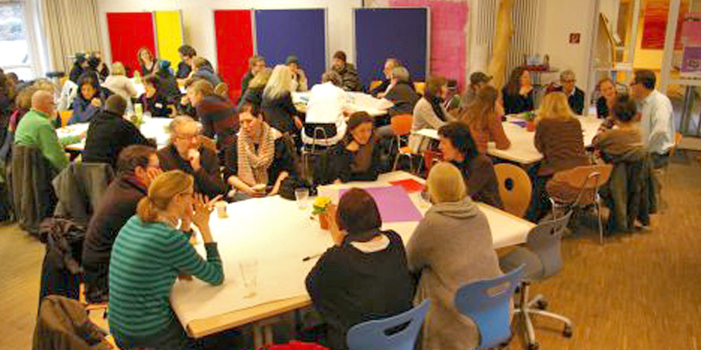 Veranstaltungsteilnehmer sind an Tischen verteilt in einem Raum der Fachschule